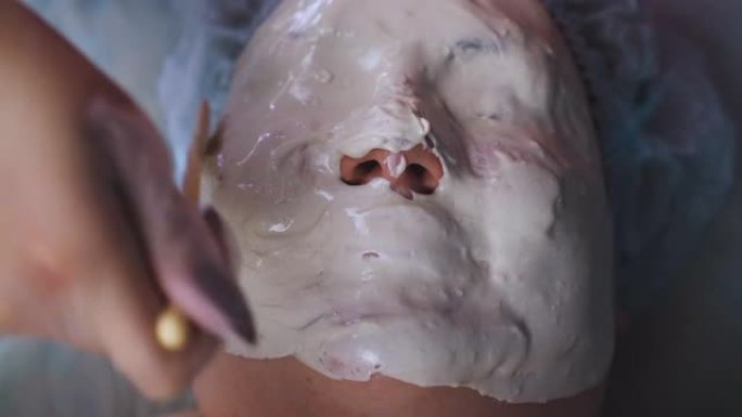 美容师在诊所用藻酸盐面膜覆盖女性面部