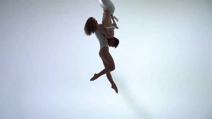 高空吊带二人组穿着白色服装，在白色背景上表演。浪漫情侣的概念