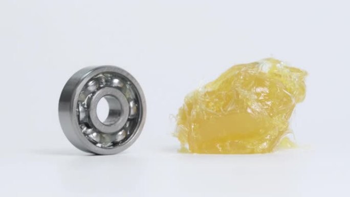 滚珠轴承在黄色锂润滑脂 (NLGI 2) 旁边旋转，并移动到白色背景上隔离的润滑脂。磨损和防锈。减少