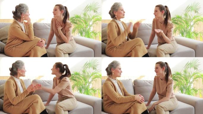 微笑的中年妇女与快乐的成年女儿在沙发上放松，谈论生活时刻。