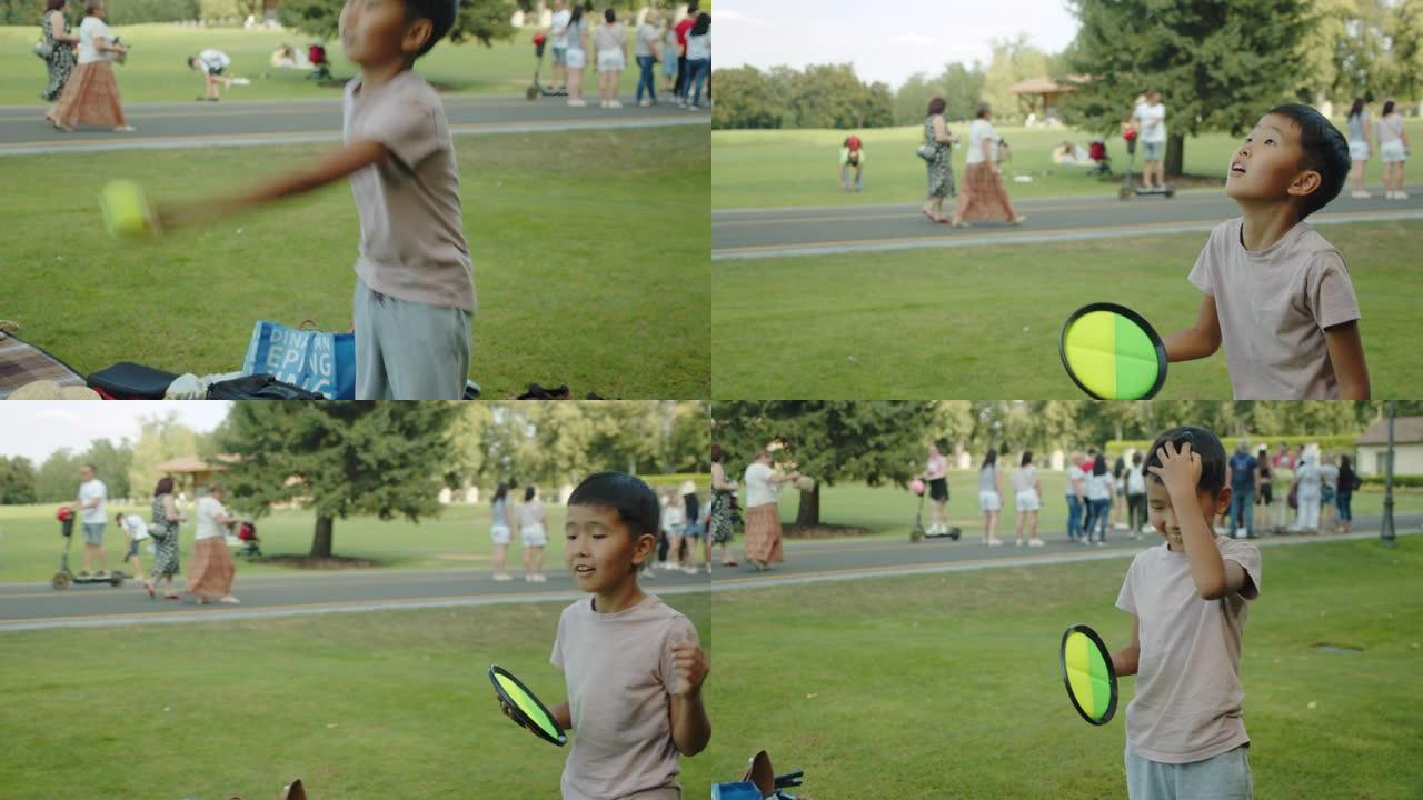 公园里的亚洲小男孩接网球，微笑，积极，笑，运动，夏天，阳光明媚，背景中的人