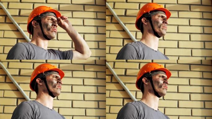 砖墙背景下的肖像肮脏建筑工人。戴着安全帽的白人英俊严肃的男人。肮脏的工作和体力劳动。工作设备的人。特
