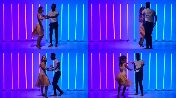 舞厅舞者在明亮的彩色霓虹灯的背景下，在工作室中练习萨尔萨舞元素。一个黑人正在跳舞一个美丽的白人女人。