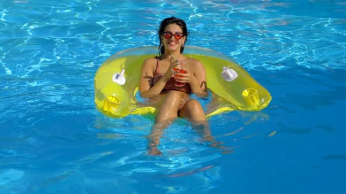 性感的女人在游泳池充气上啜饮鸡尾酒。放松，夏天