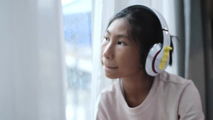 亚洲人坐在家里窗户附近的地板上，使用智能手机和耳机听音乐。