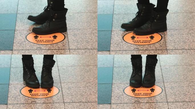 穿着黑色靴子的腿在公共场所站在 “保持距离” 的规则标志上。