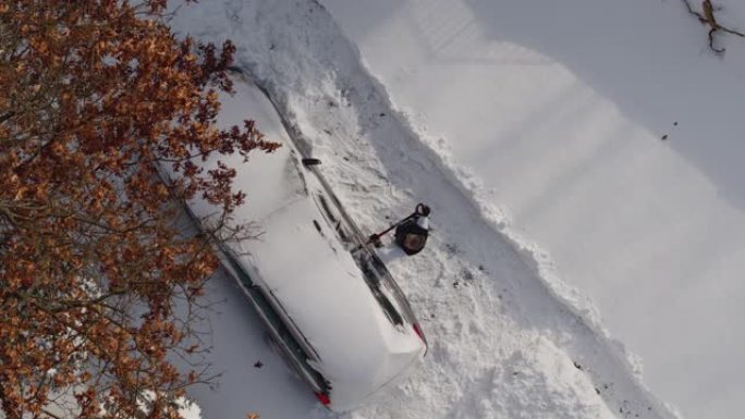 一名成年男子在冬季暴风雪后从雪地上清洗汽车。无人机视频正上方的鸟瞰图。