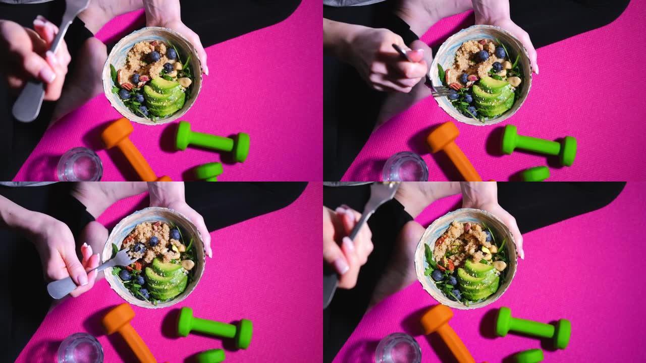 粉红色健身垫上的女人在锻炼后吃健康的素食沙拉。