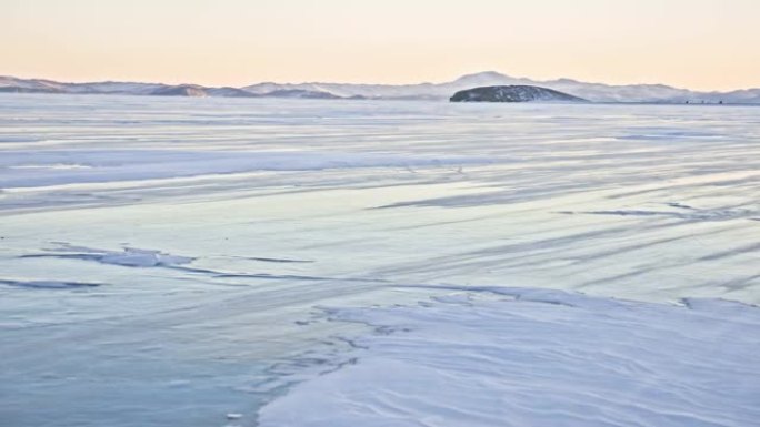 雪在冰面上飞舞。雪花在贝加尔湖的冰上飞舞。冰非常美丽，有不同寻常的独特裂缝。背景视图山景。雪闪闪发光