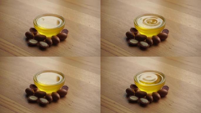 将摩洛哥坚果油放入一个玻璃碗中，并在木制背景上撒上摩洛哥坚果籽。基于摩洛哥坚果油的化妆品概念。
