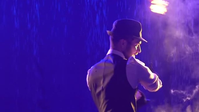 时尚的男人用链子上的发光和吸烟球表演火把戏。艺术家在蓝色烟熏工作室背景下的雨水中表演。消防和水上表演