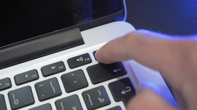 手按笔记本电脑上的power on键，特写。手指按下电源按钮打开笔记本电脑。男子正在按下笔记本电脑电
