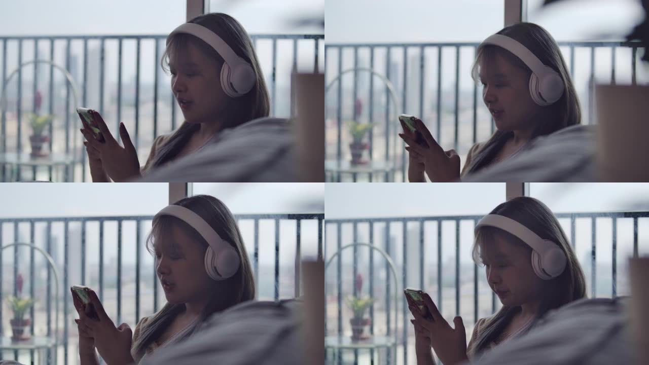 一个亚洲美丽的少女在公寓房间的客厅里用耳机和智能手机听音乐。