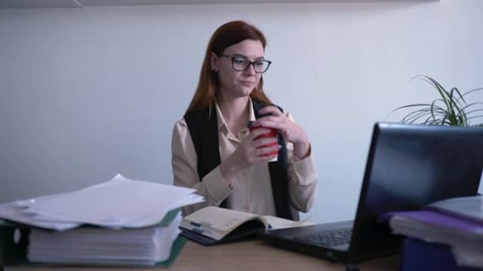 上班族，一个戴眼镜的女人，一个商业工作者在计算机上工作时喝咖啡并看着显示器屏幕，商业概念