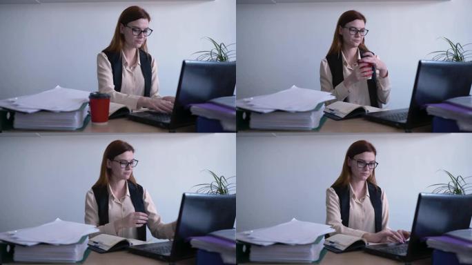 上班族，一个戴眼镜的女人，一个商业工作者在计算机上工作时喝咖啡并看着显示器屏幕，商业概念