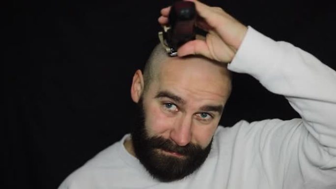 一个留着浓密胡须的男人刮胡子，用电动剃须刀去除头上的头发