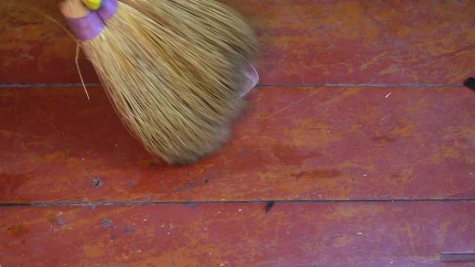 用扫帚将地板碎屑扫入塑料簸箕。用高粱扫帚扫木地板。女性家庭作业。塑料垃圾勺。家政女工。乳胶手套。打扫