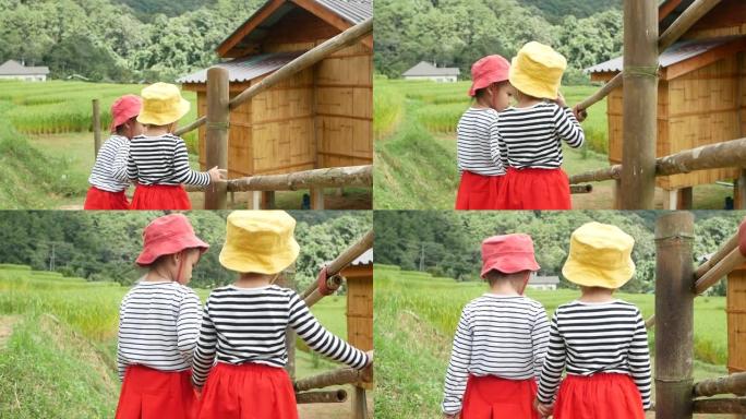 两兄妹手拉手走在一座竹桥上，看山上的水稻梯田。一家人一起度假。