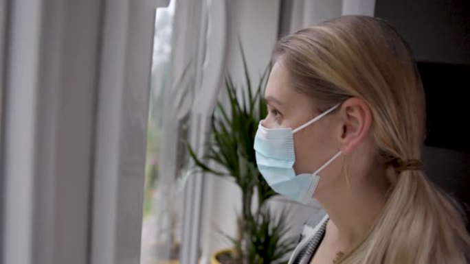 家庭检疫 -- 戴着医用口罩的年轻女子透过窗户看