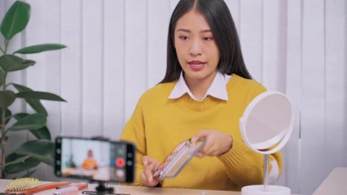 美丽的亚洲女人博主使用相机手机录制vlog视频直播并在家里化妆评论化妆品