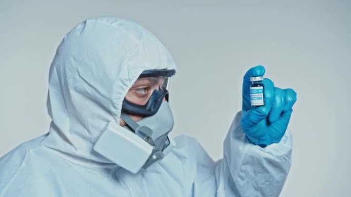 特写一位开发了冠状病毒疫苗的蒙面科学家拿着一瓶蓝色液体，并检查了疫苗。医生在用药前先看一下药