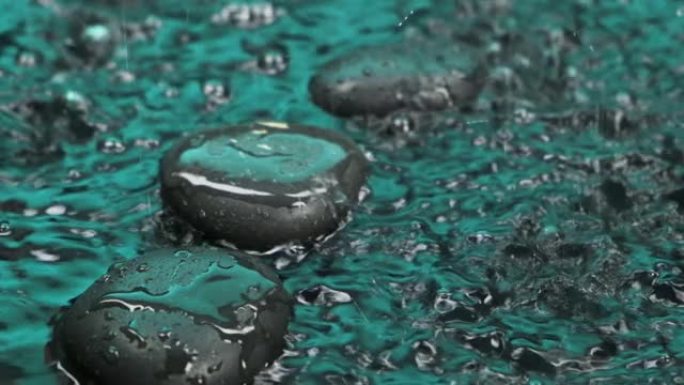 慢动作。雨开始了。雨滴落在黑色石头上的绿色水中。