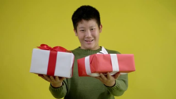 快乐的亚洲男孩穿着绿色毛衣，拿着黄色背景的礼品盒，庆祝节日或生日概念。