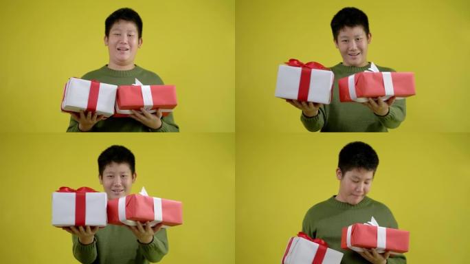 快乐的亚洲男孩穿着绿色毛衣，拿着黄色背景的礼品盒，庆祝节日或生日概念。