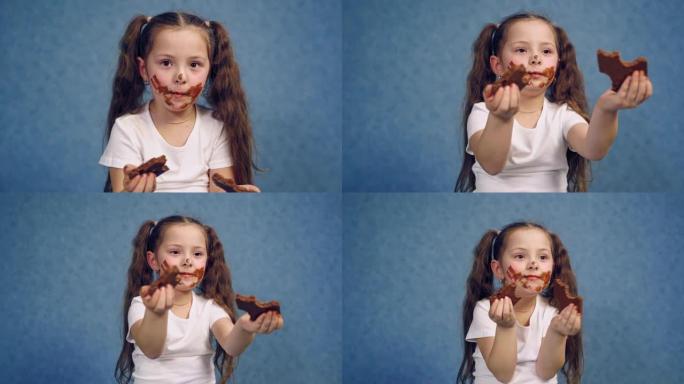 一个吃巧克力的女孩肮脏的脸。两块甜巧克力在孩子的手中。工作室里孤立的一个脸上有污迹的小孩的肖像。