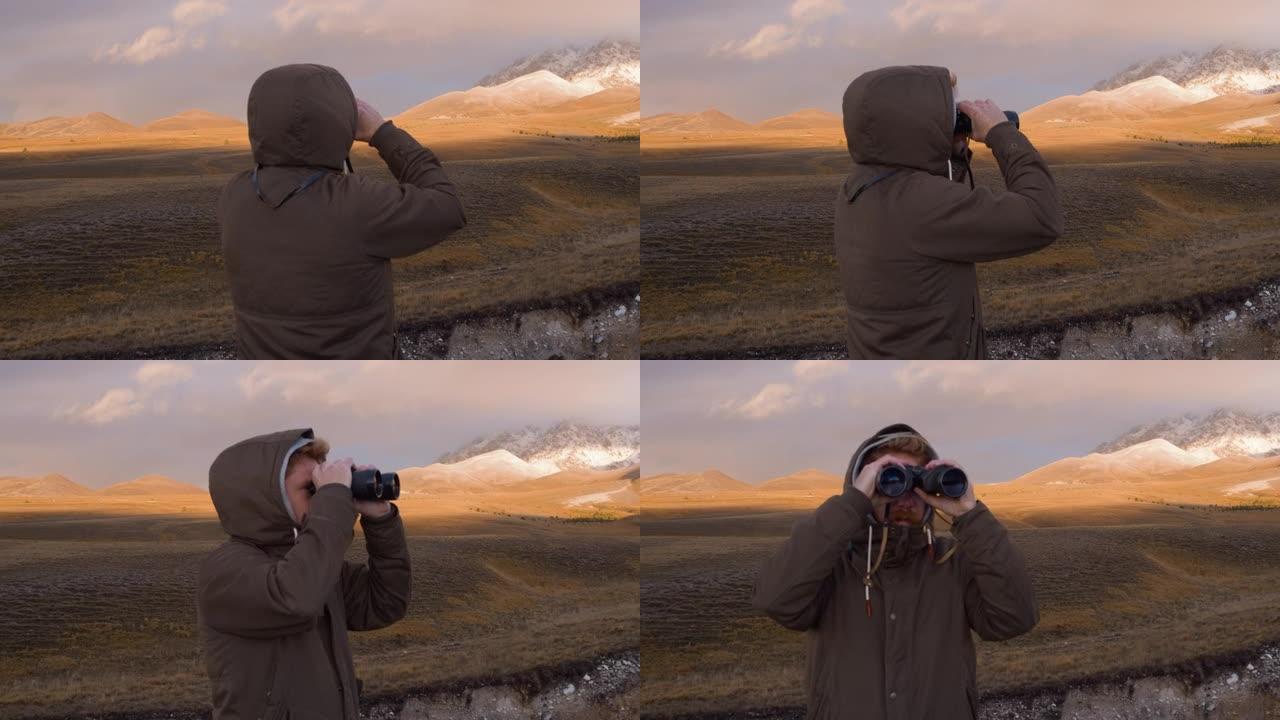 男人用双筒望远镜看，背景是山。