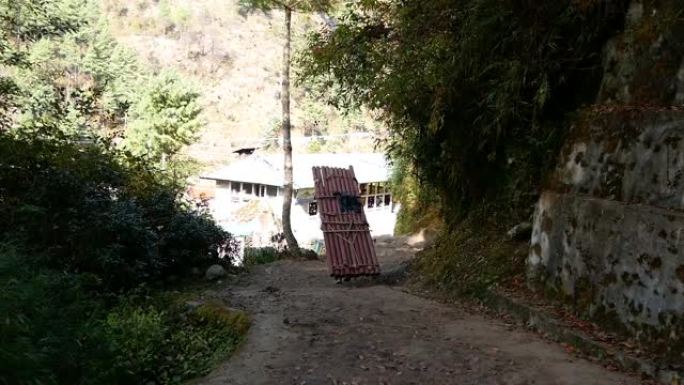 在阳光明媚的日子里，波特背着巨大的铁管在尼泊尔的夏尔巴地区昆布，背着佛教祈祷旗。