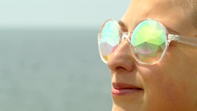 特写-海滩上戴着闪闪发光的太阳镜的美丽年轻女子的脸