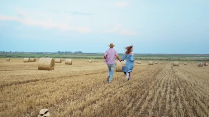 家庭周末，欢快的已婚夫妇与儿子牵着纸飞机在乡村的草堆和蓝天下奔跑