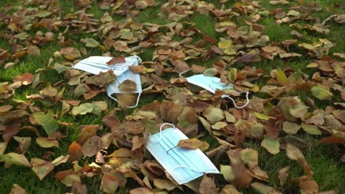 带秋叶的草地上的保护性蓝色一次性医用口罩