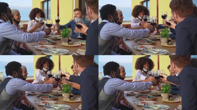 在电晕病毒大流行期间，戴着面罩的年轻多种族朋友用红酒杯敬酒