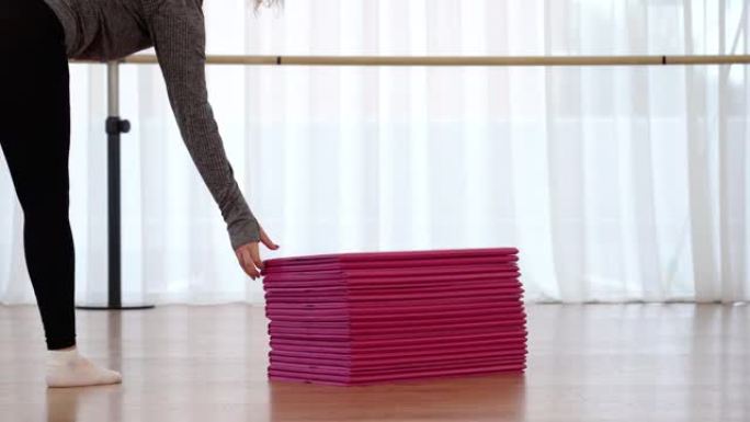 穿着紧身裤的女人带来折叠的粉红色垫子和健身房的堆叠