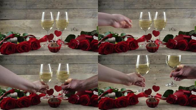 男人和女人举起他们的眼镜。酒杯和酒，木桌背景上的红玫瑰。喝红酒，庆祝一下。情人节。4k快照