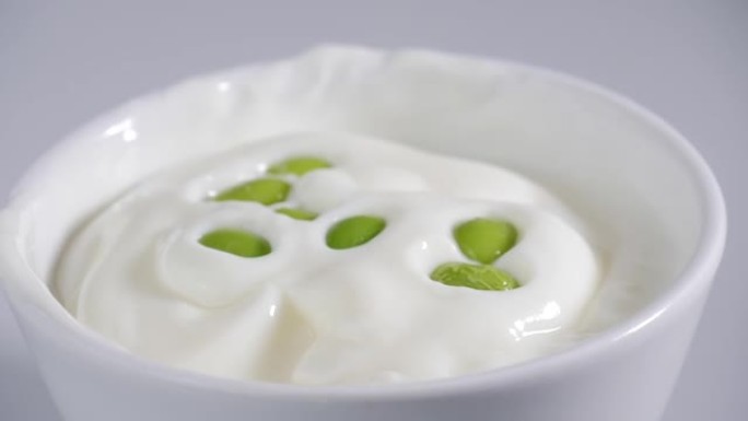 绿色大豆落在酸奶碗上，慢动作。