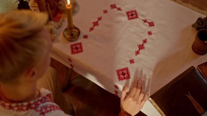 美丽的绣花桌布躺在桌子上，一个男人打开一本关于斯拉夫文字的旧书。蜡烛和护身符摆在斯拉夫人的餐桌上，文