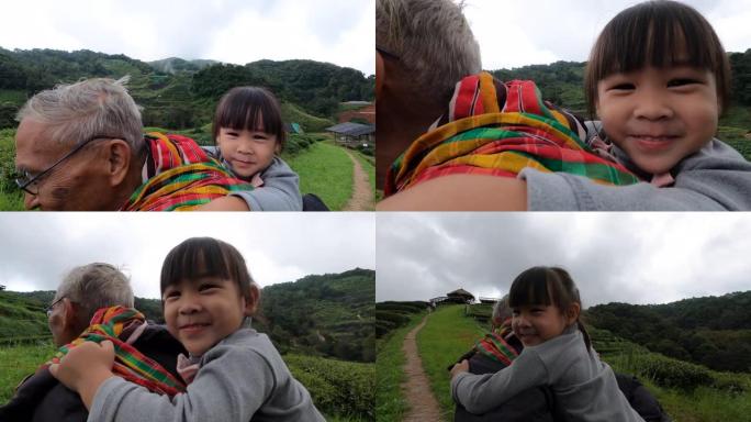 可爱的小孙女背着她的祖父，早晨在温和的阳光下漫步并欣赏山上的茶园。