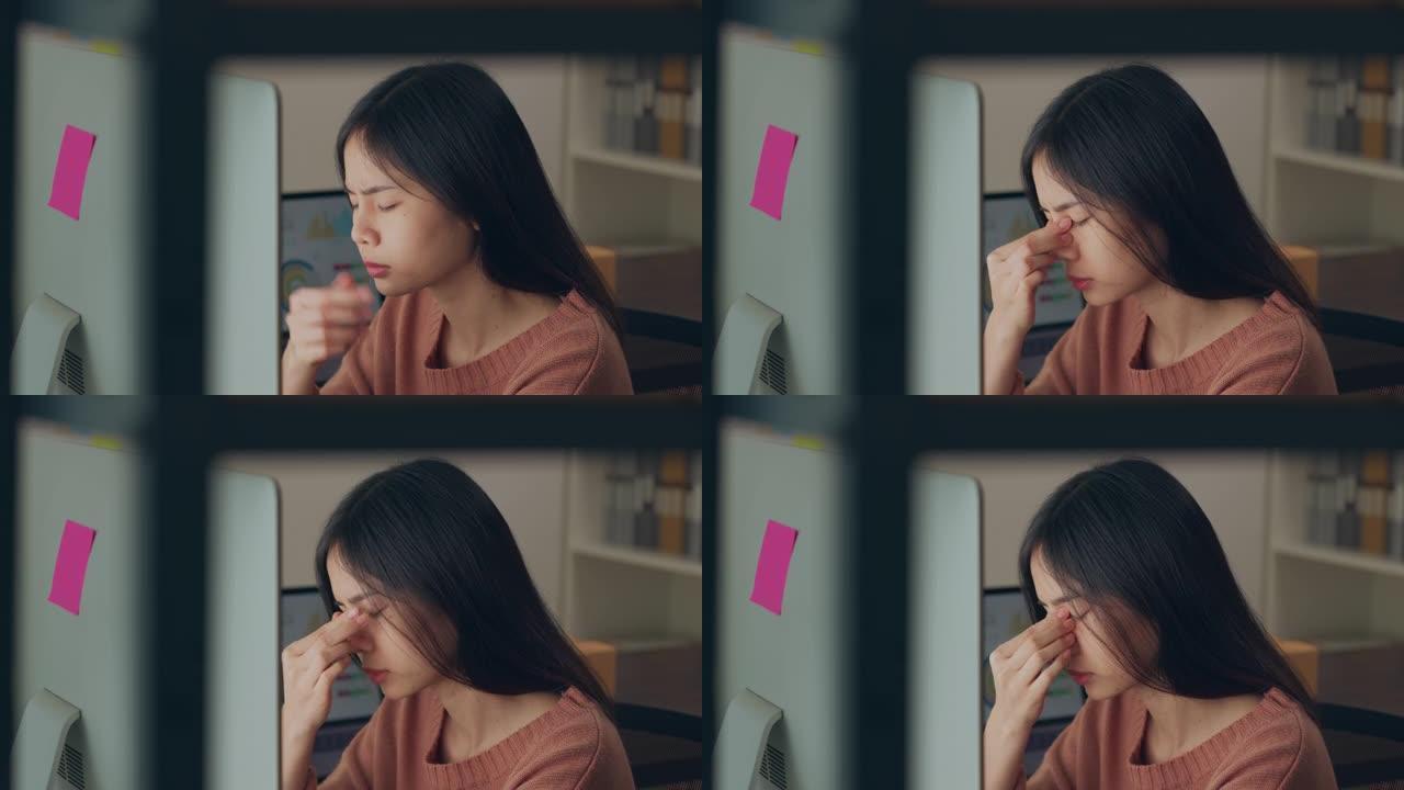 疲倦的年轻亚洲妇女使用笔记本电脑，长时间工作后在家庭办公室感到眼睛疲劳。