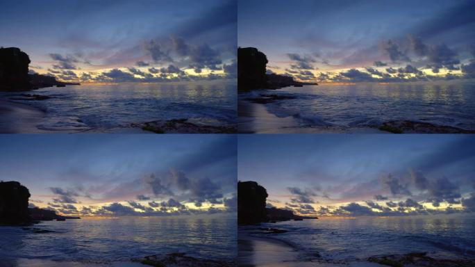岩石海滩，潮汐高潮，日落后深蓝色的水，在岩石的热带岛屿上