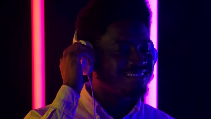 一位年轻时尚的非洲裔美国男性戴着白色大耳机微笑着享受音乐的肖像。特写。慢动作