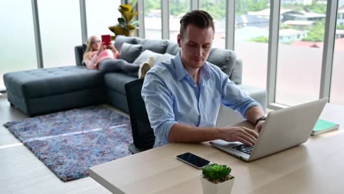 年轻情侣恋人穿着休闲装一起在家里的客厅笔记本电脑上工作的快乐和放松的生活方式。