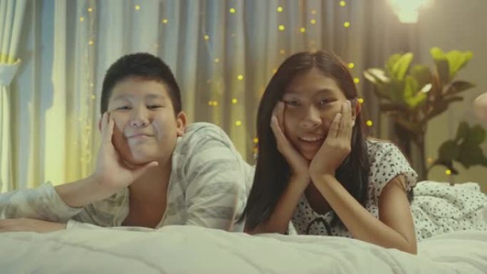 快乐的亚洲男孩和他的妹妹在晚上一起在床上拥抱。生活方式概念。