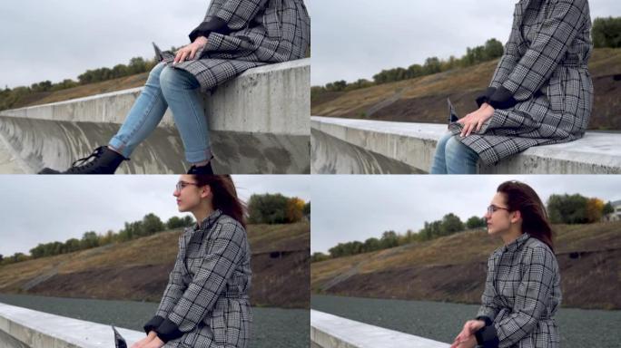 年轻女子坐在风中的水泥栅栏上，摇晃双腿