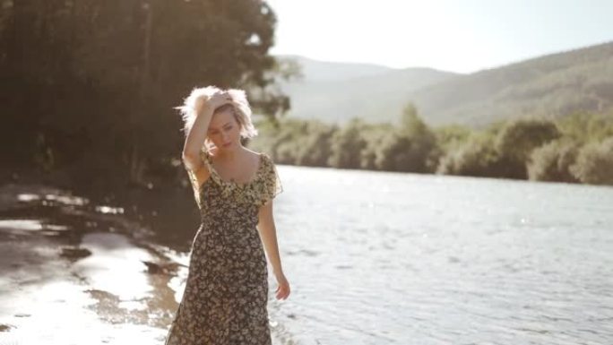 美丽的金发女孩在河边阳光明媚的日子里用相机调情