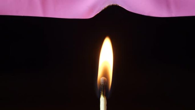 粉红色的聚氯乙烯薄片燃烧并在黑色背景上隔离的火柴火焰上吸烟的微距拍摄。4k 50 fps慢动作