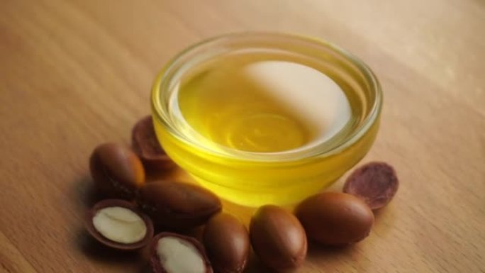 将摩洛哥坚果油放入一个玻璃碗中，并在木制背景上撒上摩洛哥坚果籽。基于摩洛哥坚果油的化妆品概念。