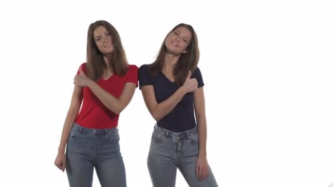 年轻的高加索双胞胎姐妹的肖像用相反的手竖起大拇指。孤立在白色背景上